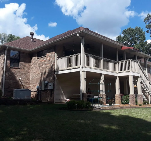 Two-story brick house with a covered balcony and white columns under a blue sky