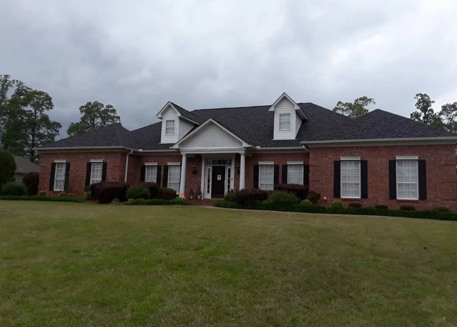 Single-story brick house with a dark roof and large front lawn on an overcast day