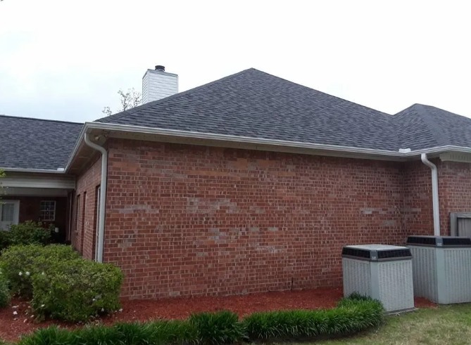 Brick suburban house exterior with dark shingled roof and shrubs along the front yard