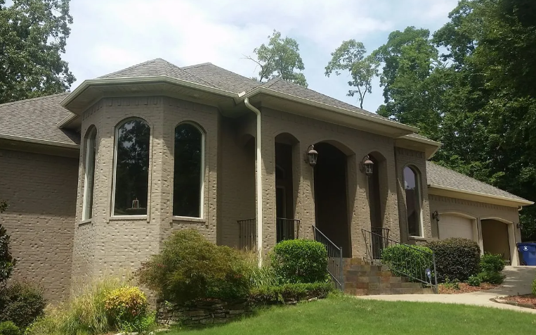 Suburban brick house with arched windows, front porch, and landscaped yard surrounded by trees
