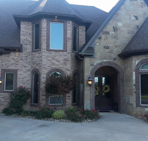 Brick house exterior with arched entryway, tall windows, and a driveway in front
