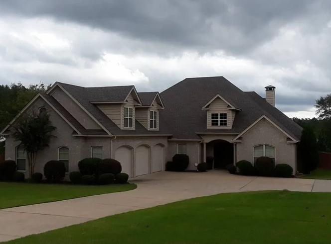 Large gray suburban house with a three-car garage and curved driveway under cloudy skies