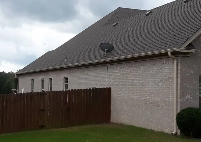 Gray house with a dark roof and satellite dish behind a wooden fence under cloudy skies
