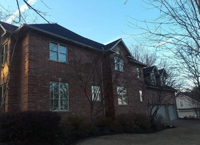 Red-brick apartment building with bare trees and a driveway under a clear blue sky