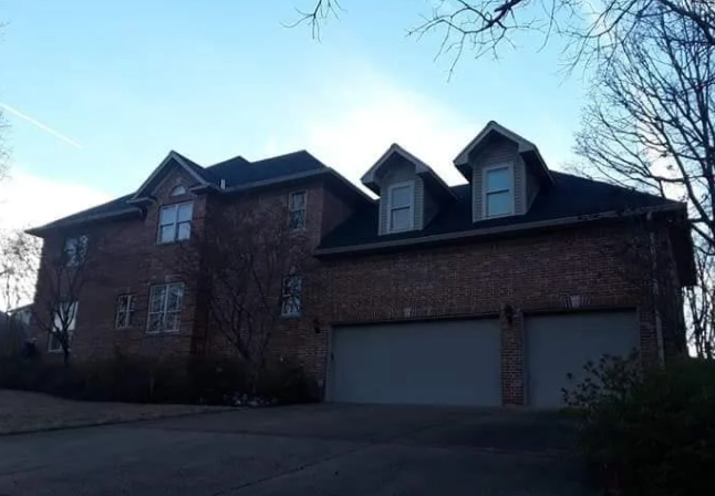 Brick suburban house with two garage doors and dormer windows at dusk