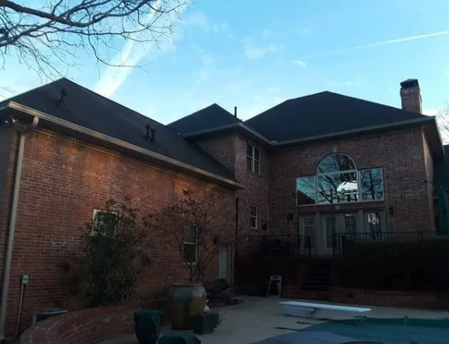 Brick house exterior with a backyard patio and pool under a clear evening sky