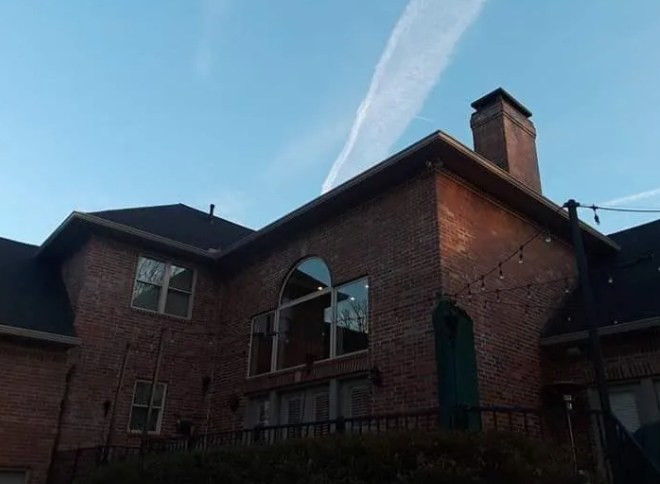 Brick house exterior at dusk with arched window and chimney under a blue sky.