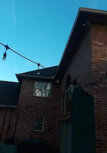 Brick building exterior at dusk with a dark doorway, windows, and string lights against a blue sky