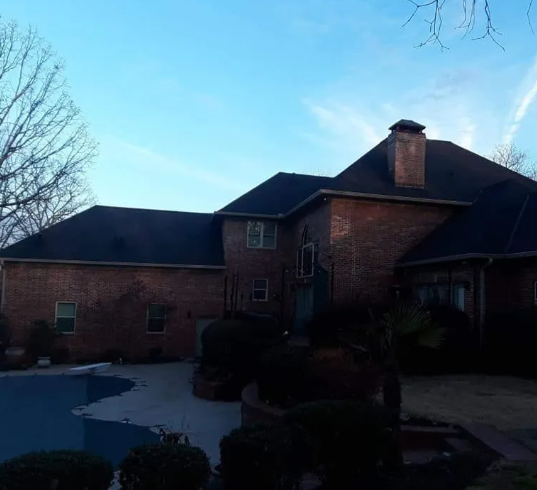 Brick house exterior with dark roof, chimney, and driveway under a clear blue sky