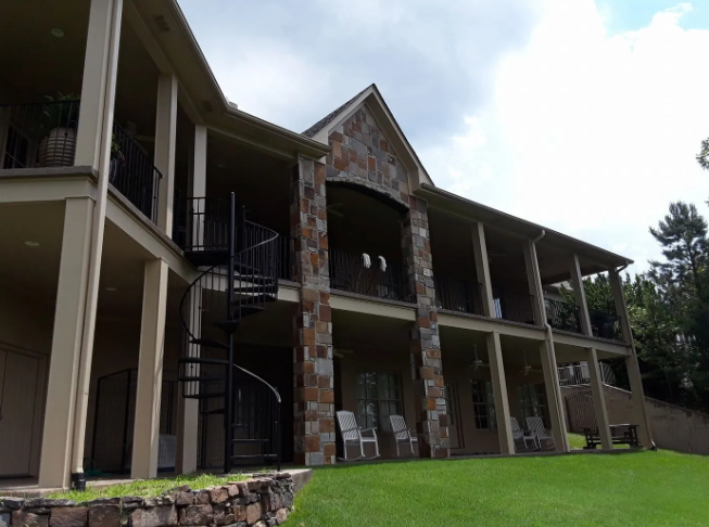 Stone-and-wood apartment building with balconies and a spiral staircase beside a green lawn.