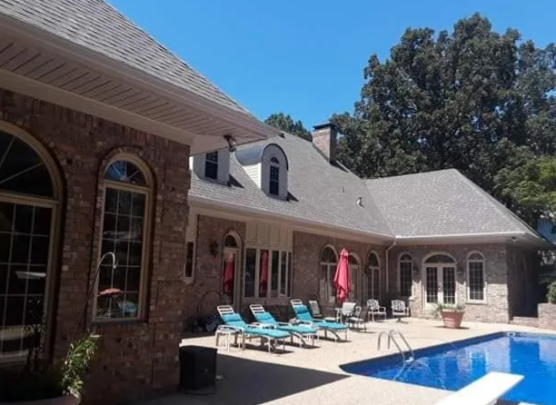 Brick house patio with blue lounge chairs and a swimming pool under a sunny sky