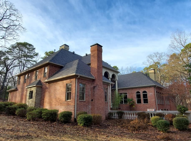 Brick Tudor-style house with dark roof, arched windows, and autumn trees in the yard