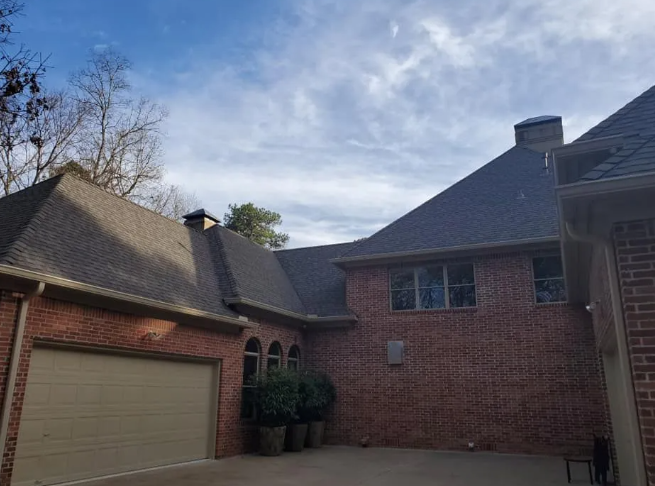 Brick house courtyard with garage, steep shingled roofs, and trees under a blue sky