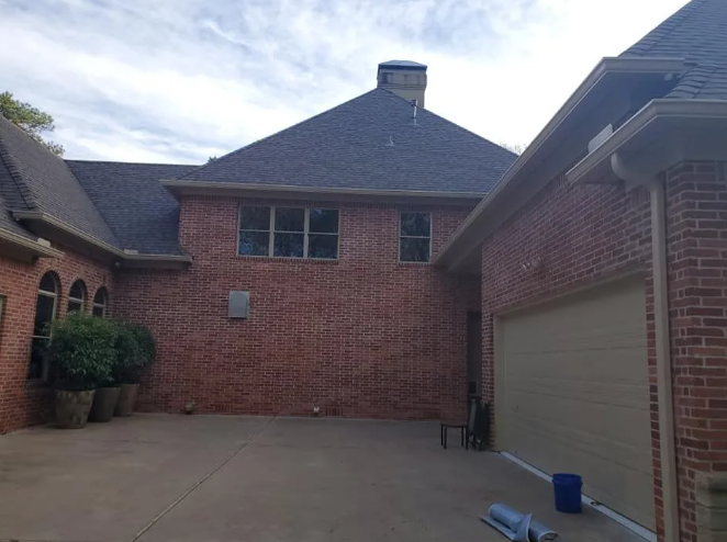 Brick house courtyard with concrete driveway, beige garage door, and blue bins on the right.