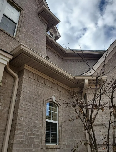 Brick house exterior with a window, roofline, and bare tree branches against a cloudy sky
