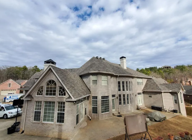 Large gray shingle-style house with dormer windows under a cloudy sky, viewed from the front-left.