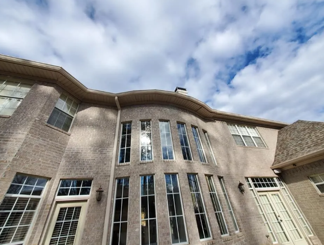 Curved brick house exterior with tall windows and a cloudy sky above