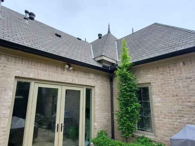 Stone patio courtyard with double doors, pitched gray roofs, and a tall green vine on the right wall