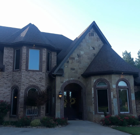 Stone house exterior with arched windows, steep roof, and a driveway at dusk