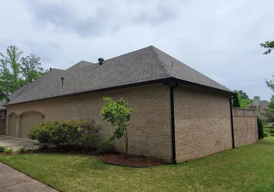 Single-story brick house with gray shingled roof and a small landscaped yard under cloudy skies