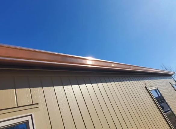 Side of a tan building with a brown roof edge against a bright blue sky