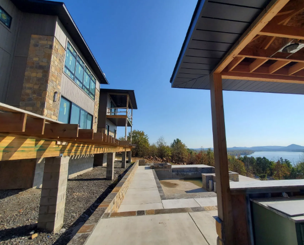 Modern lodge terrace with stone walkway, wooden beams, and lake view under a clear blue sky