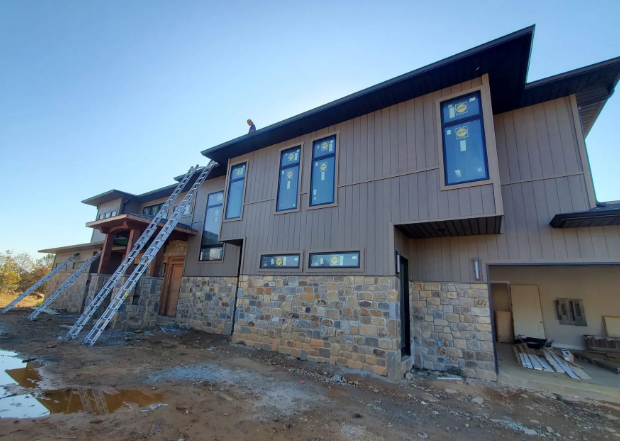 Two-story house under construction with ladders, stone lower walls, and unfinished ground outside
