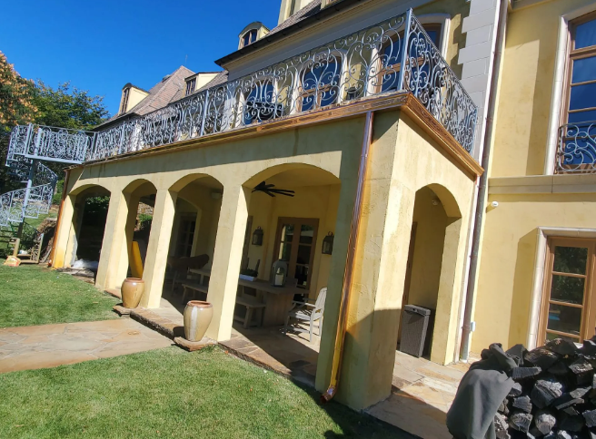 Yellow villa with arched porch, blue balcony railings, and a green lawn in front