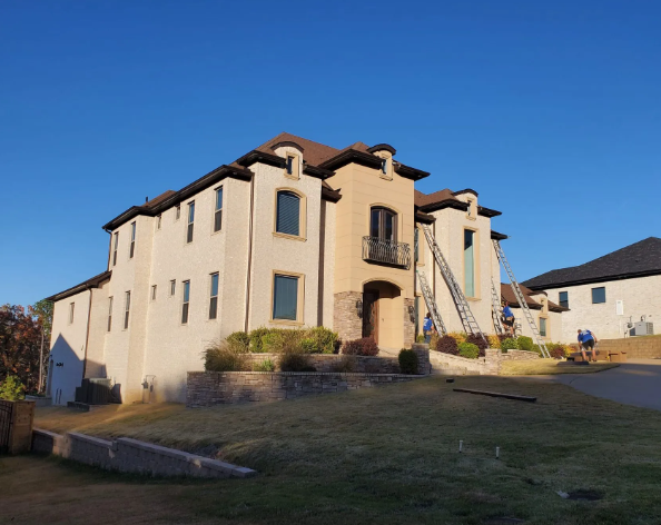Tan stucco apartment building with brown trim on a grassy slope under a clear blue sky