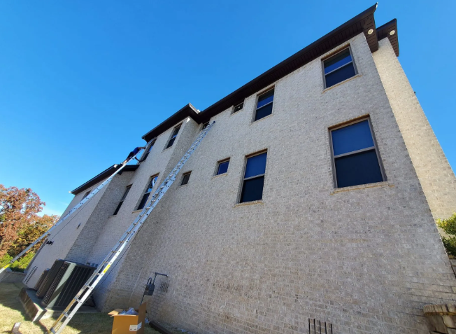 Tall beige apartment building viewed from below against a clear blue sky.