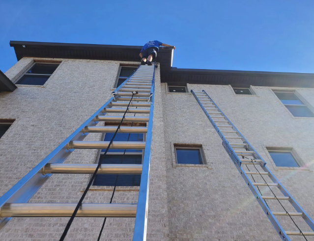 Person on top of a long ladder against a white building with a blue sky background