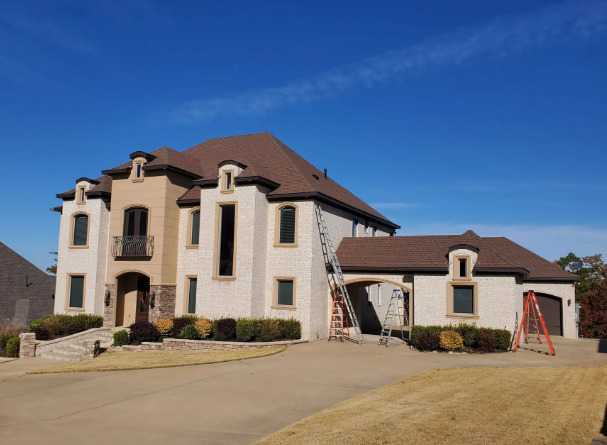 Large cream-colored house with brown roof and front driveway under a clear blue sky