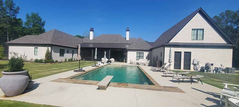 Backyard with a swimming pool and beige house, patio chairs, and a sunny lawn