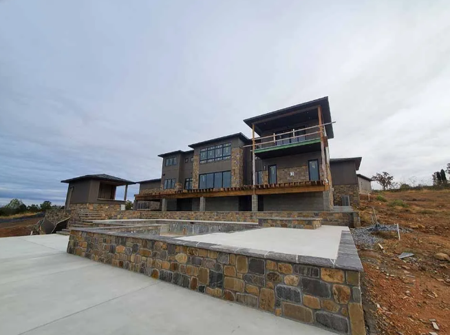 Modern stone-and-wood house under construction with a large concrete driveway and retaining wall