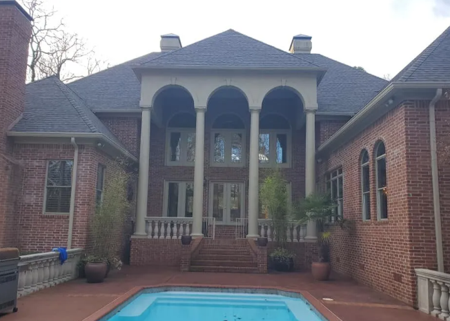 Brick house courtyard with a turquoise pool and covered balcony upstairs