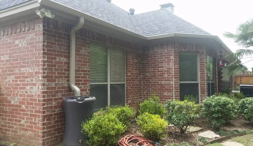 Brick house exterior with windows, gutter downspout, and shrubs in the front yard