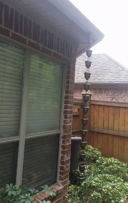 Rainy backyard patio with brick wall, sliding glass door, fence, and a tall stacked bird feeder/pole