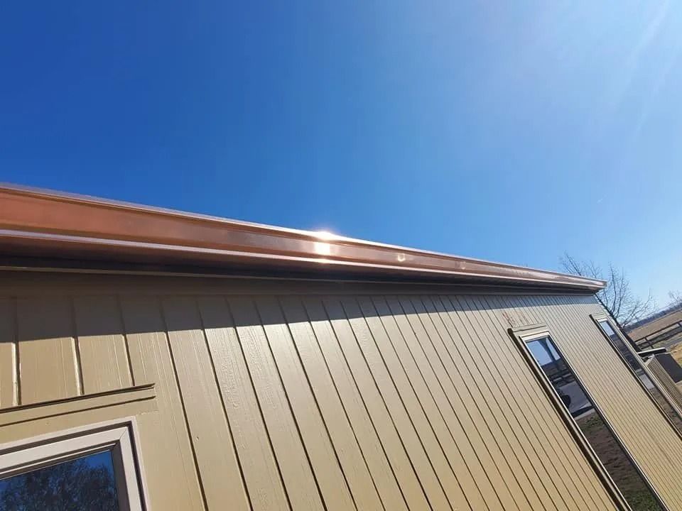 Beige house wall with brown roof under a clear blue sky, viewed from below