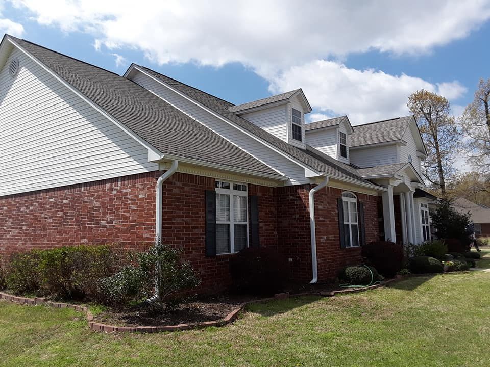Brick house with white siding and red brick exterior, viewed from the front lawn on a sunny day.
