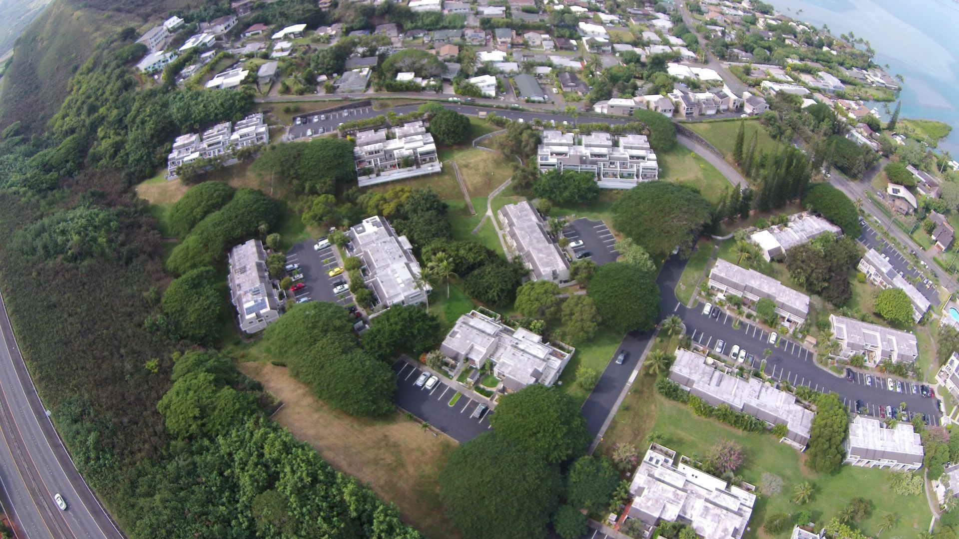 Aerial view of apartment buildings surrounded by trees and a roadway near a body of water.