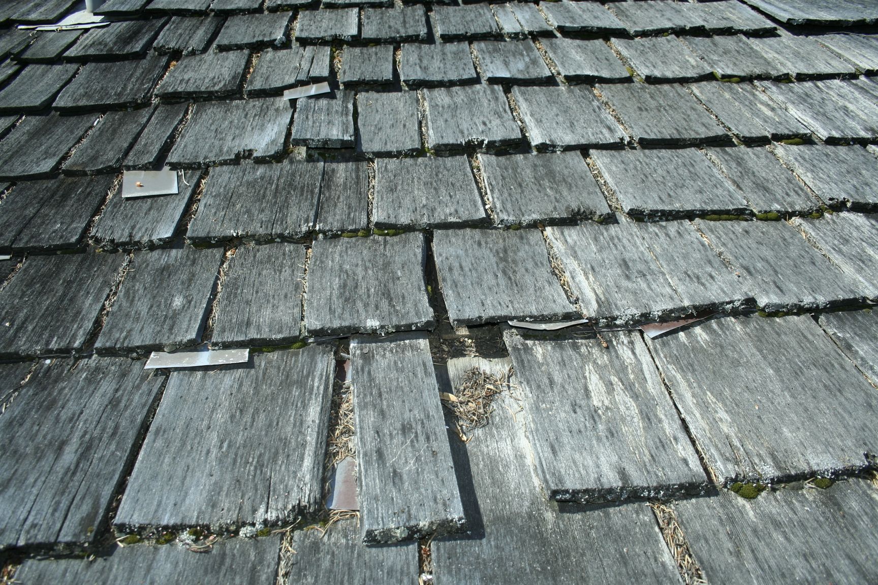 Close-up of weathered wooden roof shingles, some broken or missing, showing signs of wear and tear.