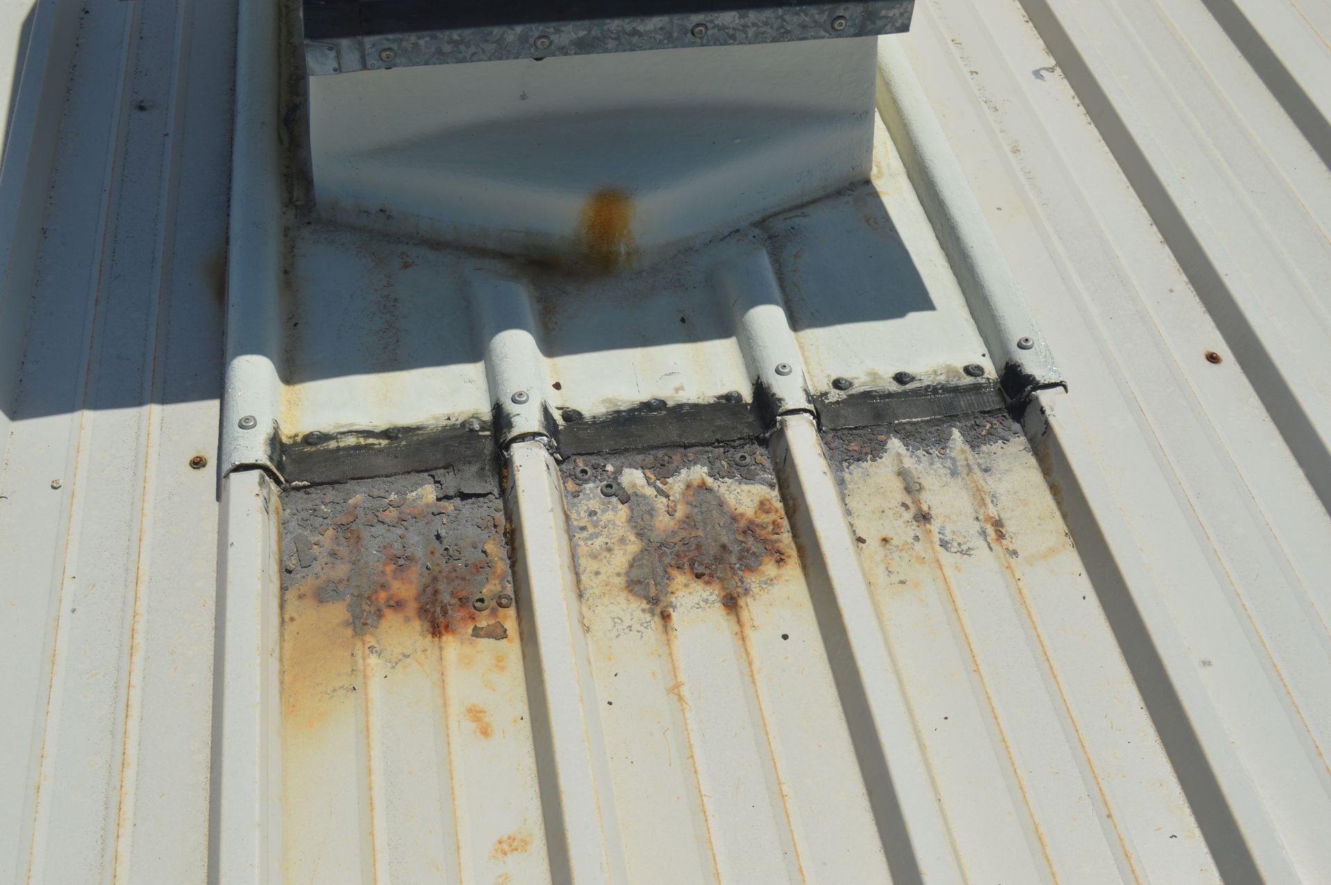 White metal roof with rust and sealant degradation around a vent.