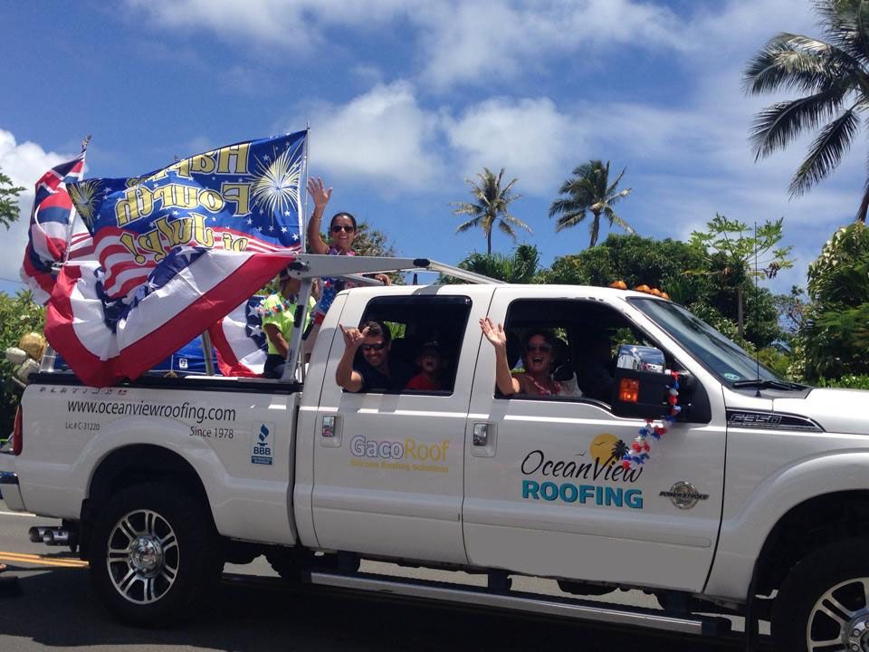 White pickup truck in a parade, waving people, American flag, OceanView Roofing logo.