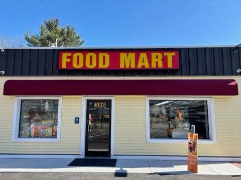 Street view of a small convenience store with a yellow facade, red awning, and signage. Bright, sunny day with a clear blue sky.