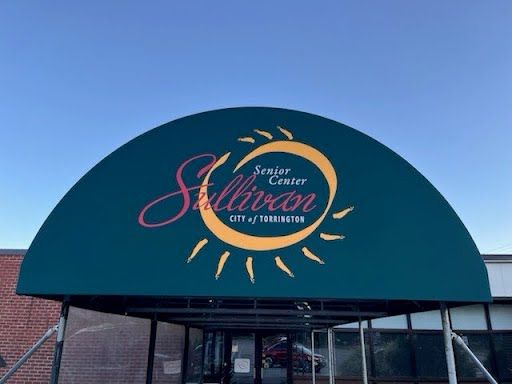 Green entrance canopy with yellow and red lettering. Background features a clear blue sky.