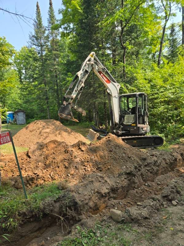 Mini excavator digging a dirt pile in a wooded construction area.