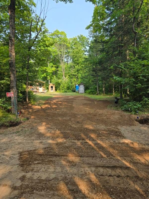 Dirt road through a wooded area with small buildings and a blue portable toilet ahead.