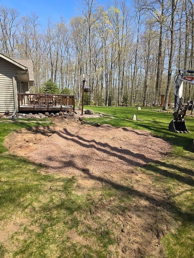 Backyard with muddy slope, wooden deck, and leafless trees under a clear sky