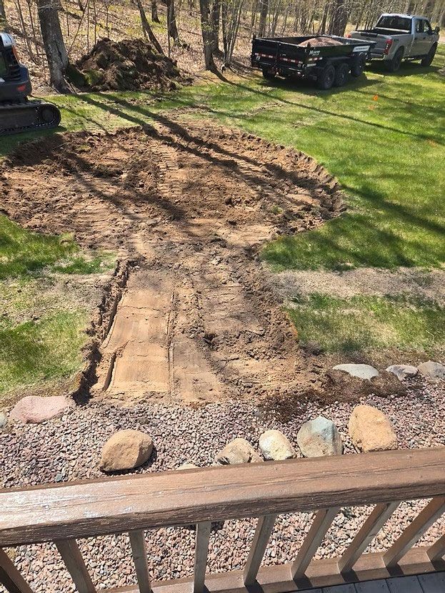 A muddy backyard with a dirt path, grass patches, stones, and a wooden railing in the foreground.