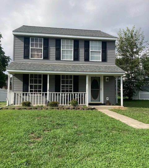 A large gray house with black shutters and a large lawn in front of it.